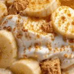 Bowl of high protein banana pudding topped with banana slices and crushed shortbread cookies