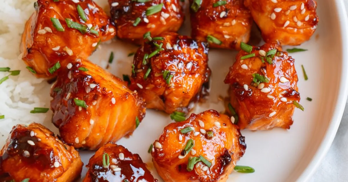 Teriyaki salmon bites with sesame seeds and chopped herbs on a white plate with rice