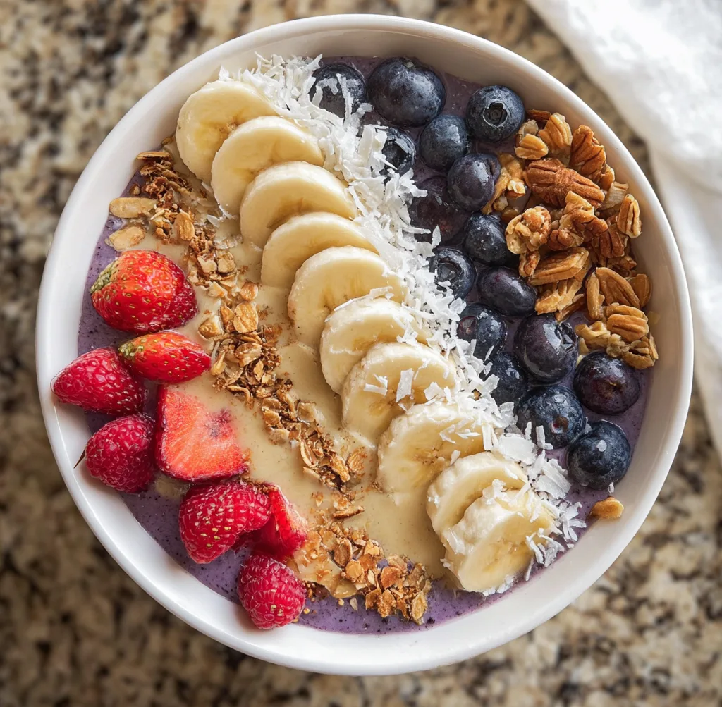 blueberry banana smoothie bowl topped with pecans, coconut and strawberries