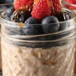 Blended oats topped with raspberries, blueberries, and honey in a glass jar